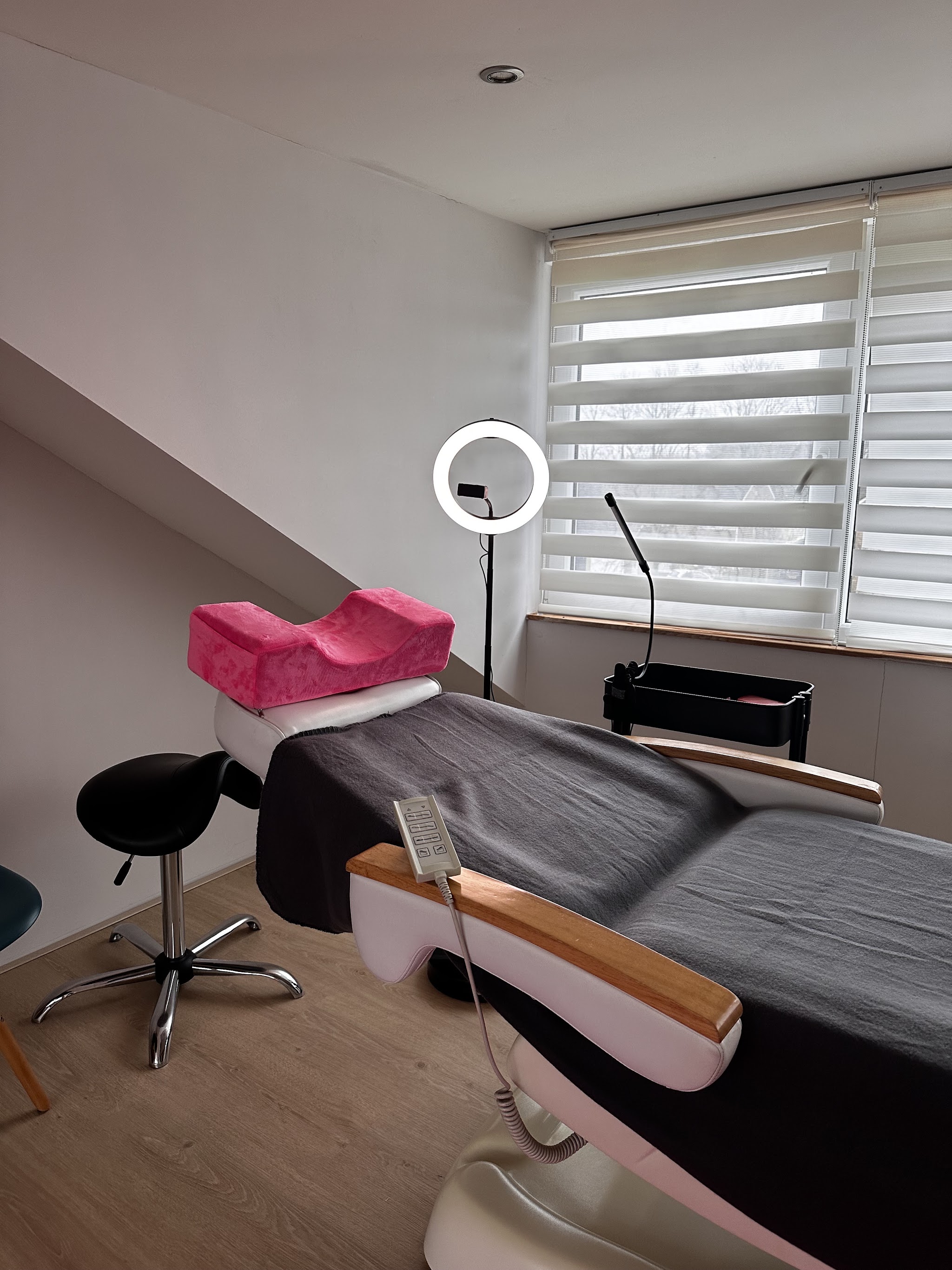 Behandelstoel met roze kussen en een ringlamp onder het schuine plafond